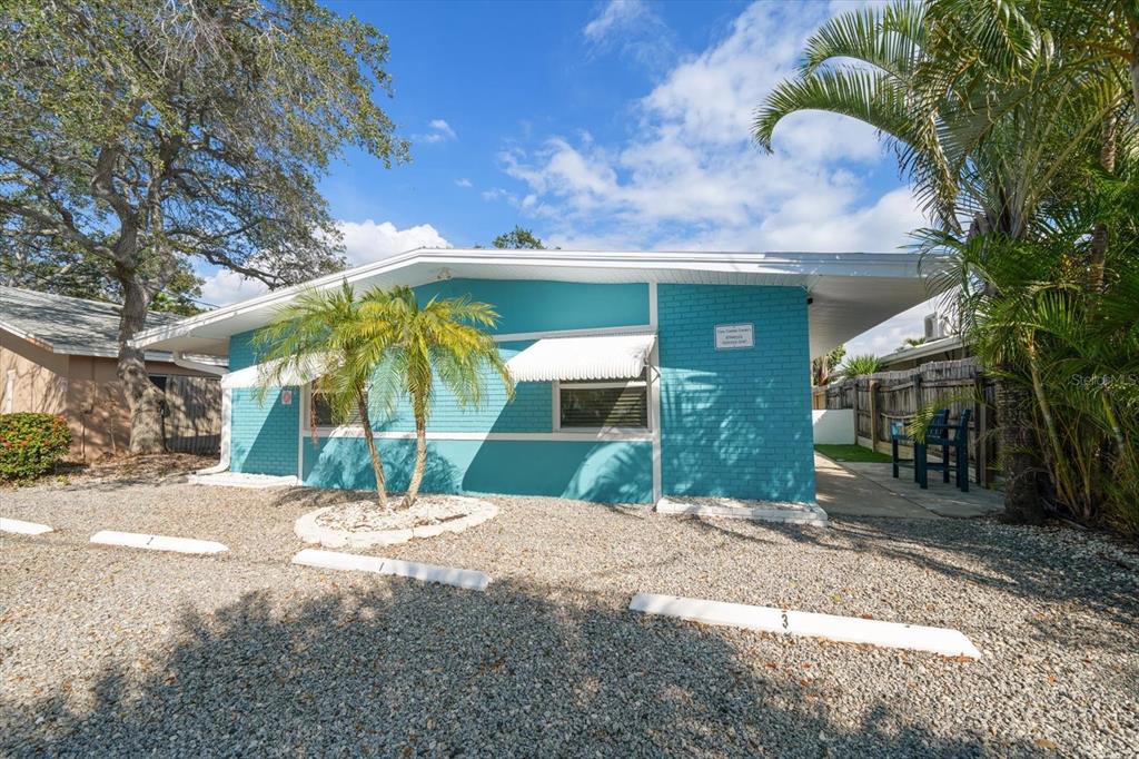 A turquoise, single-story brick building with white awnings sits behind a gravel parking area — 711 E GULF BOULEVARD, INDIAN ROCKS BEACH, FL