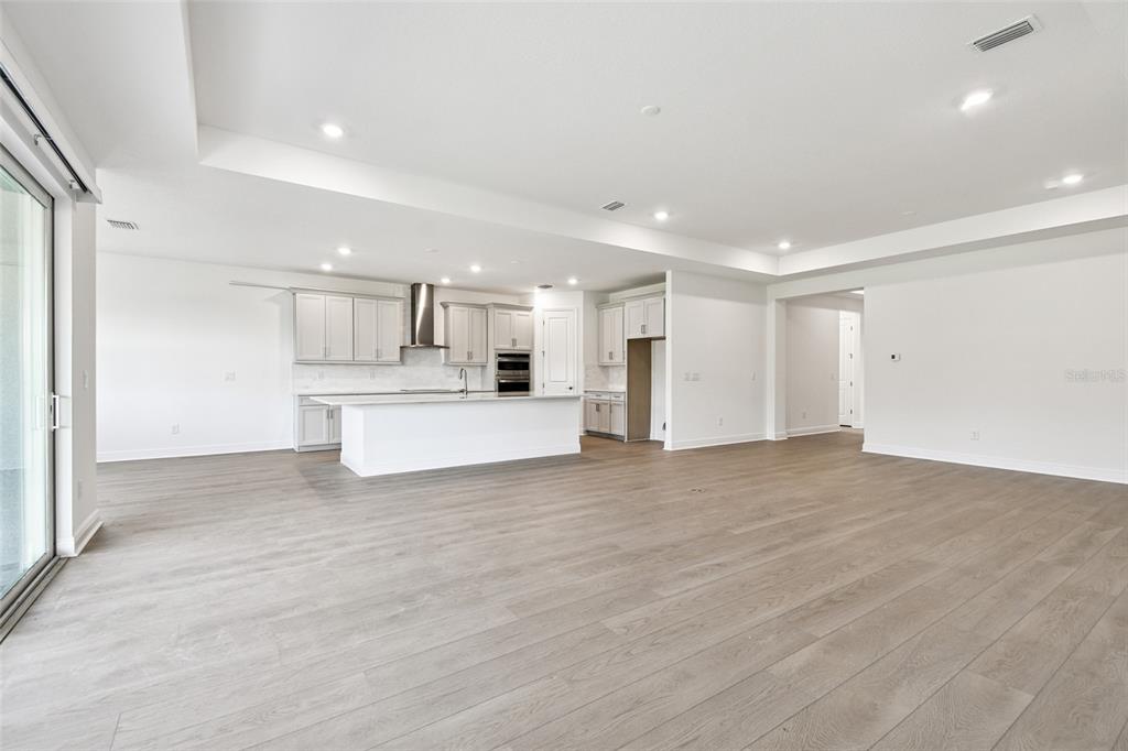 An open-concept kitchen features light gray cabinetry, a central island, and wood-look flooring — 3673 142ND TER E, PARRISH, FL