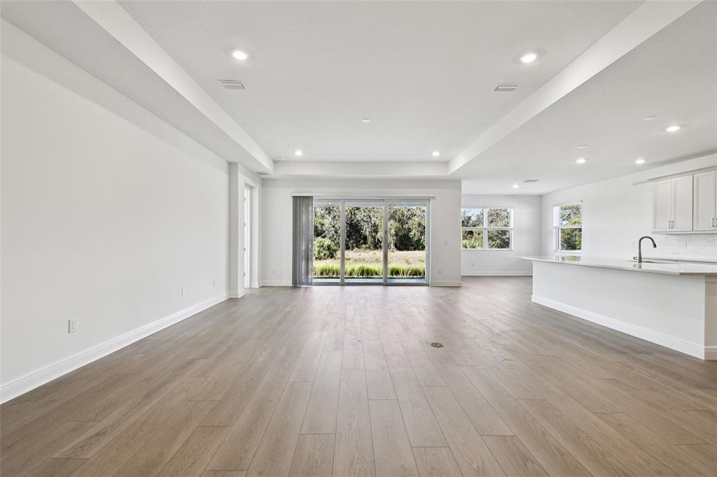 An open-concept living area features light wood-look flooring, white walls, and a modern kitchen — 3673 142ND TER E, PARRISH, FL