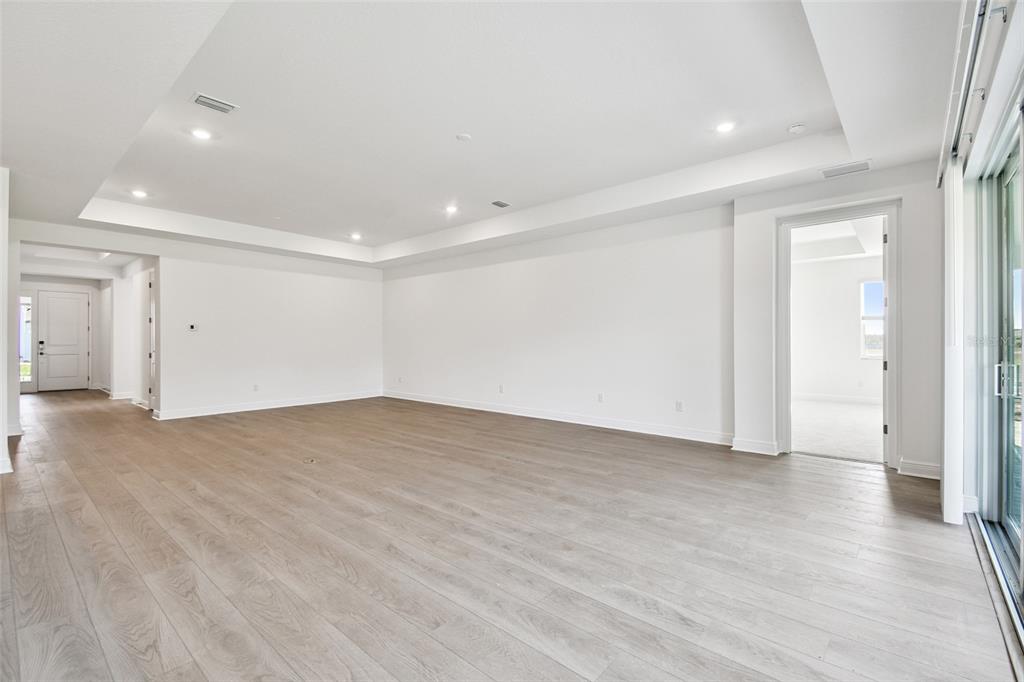 An empty living room features light wood-look flooring, white walls, and a tray ceiling — 3673 142ND TER E, PARRISH, FL
