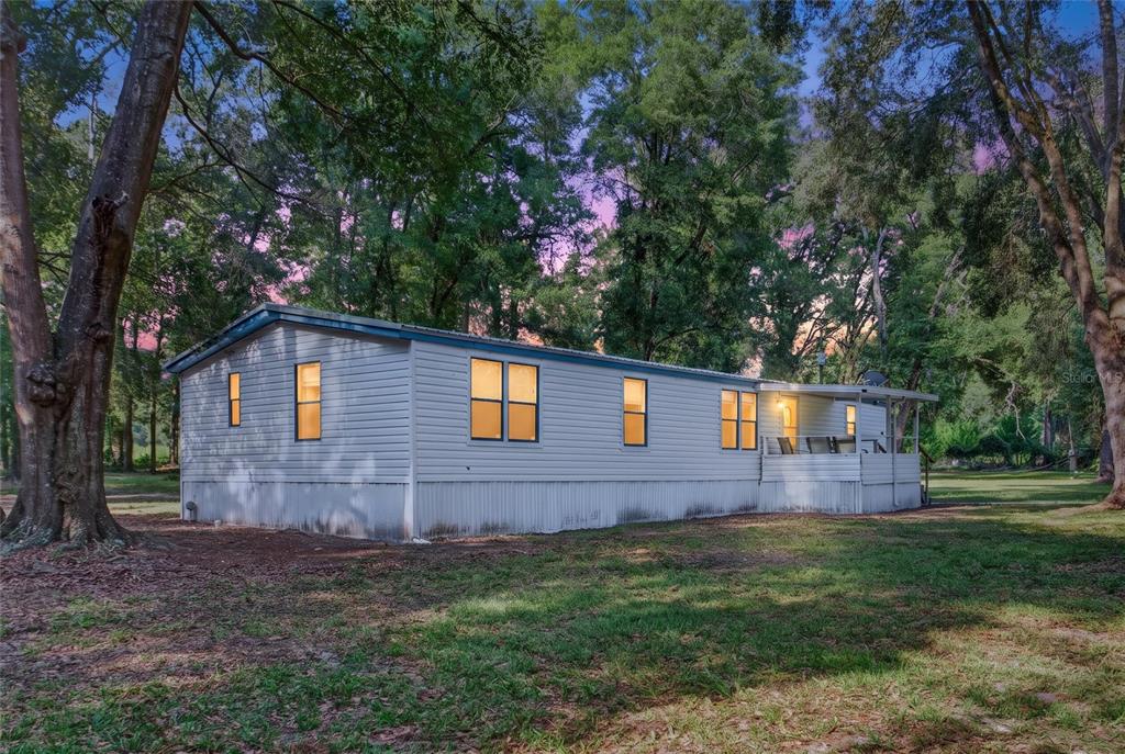 A light-colored mobile home sits on a grassy lot surrounded by tall trees at dusk — 304 COLGATE LOOP, FORT WHITE, FL