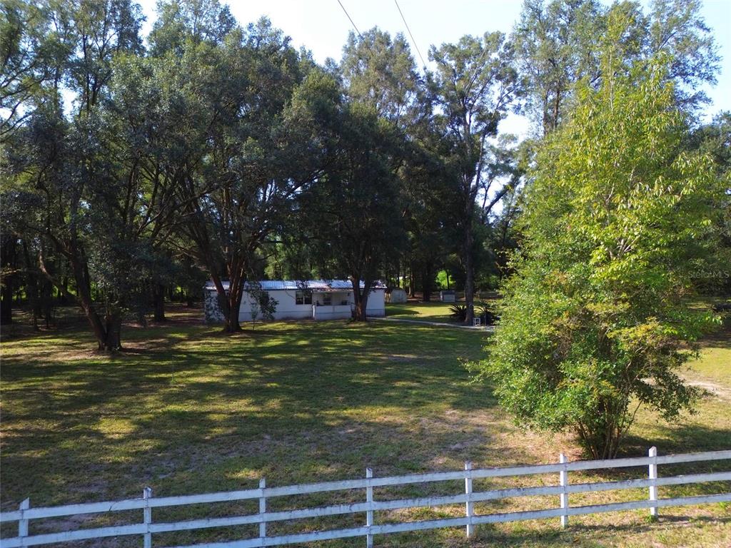 A white house sits on a large, grassy lot surrounded by many mature trees — 304 COLGATE LOOP, FORT WHITE, FL