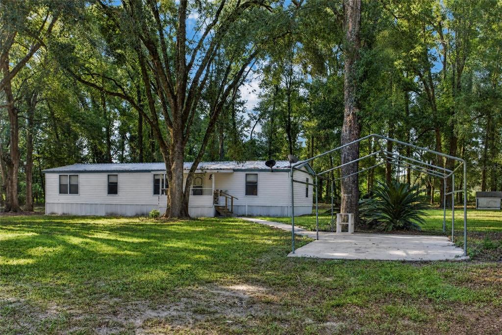 A white mobile home sits on a grassy lot with a metal carport structure nearby — 304 COLGATE LOOP, FORT WHITE, FL