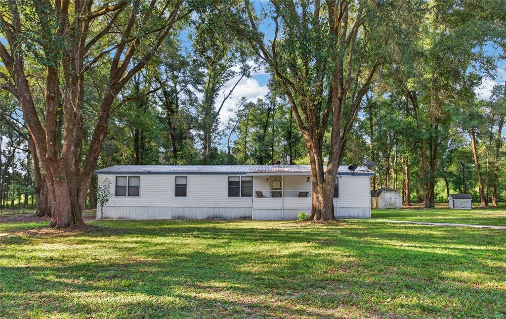 A single-story mobile home with white siding sits on a grassy lot among many trees — 304 COLGATE LOOP, FORT WHITE, FL
