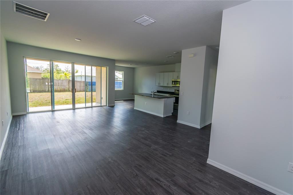 An open-concept living area features dark wood-look flooring, a kitchen island, and sliding glass doors — 1348 PALAU STREET SE, PALM BAY, FL