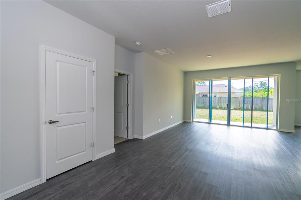 An empty room features gray walls, dark wood-look flooring, and a large sliding glass door — 1348 PALAU STREET SE, PALM BAY, FL