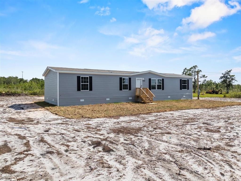 A gray manufactured home with black shutters sits on a sandy, undeveloped lot — 8457 N CAROUSEL TERRACE, CRYSTAL RIVER, FL