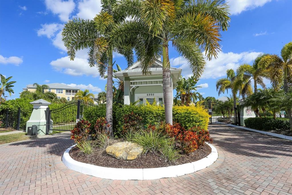 A gated entrance features a small guardhouse, palm trees, and a brick-paved driveway — 10640 LEMON CREEK LOOP UNIT 101, ENGLEWOOD, FL