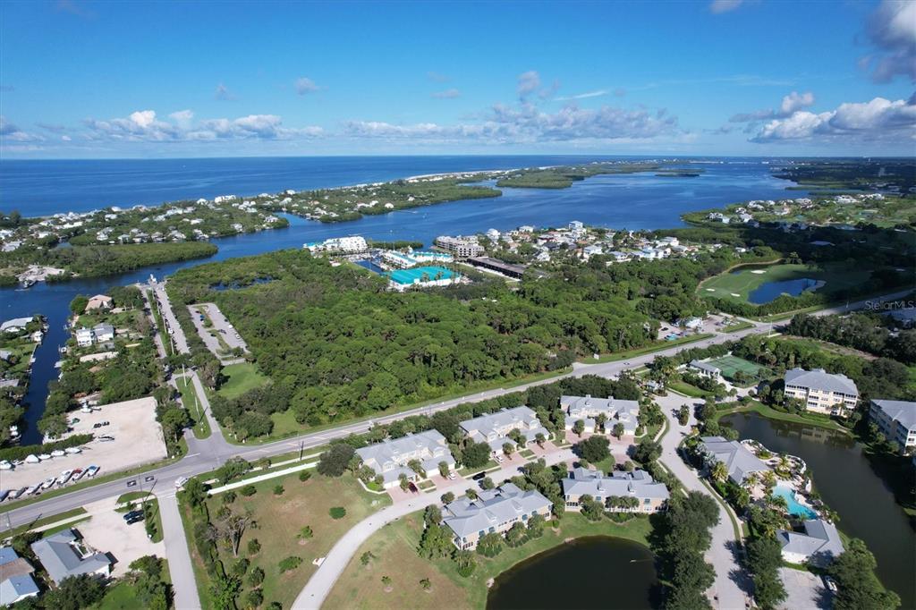 An aerial view shows a coastal residential community with lush greenery, ponds, and nearby water — 10640 LEMON CREEK LOOP UNIT 101, ENGLEWOOD, FL