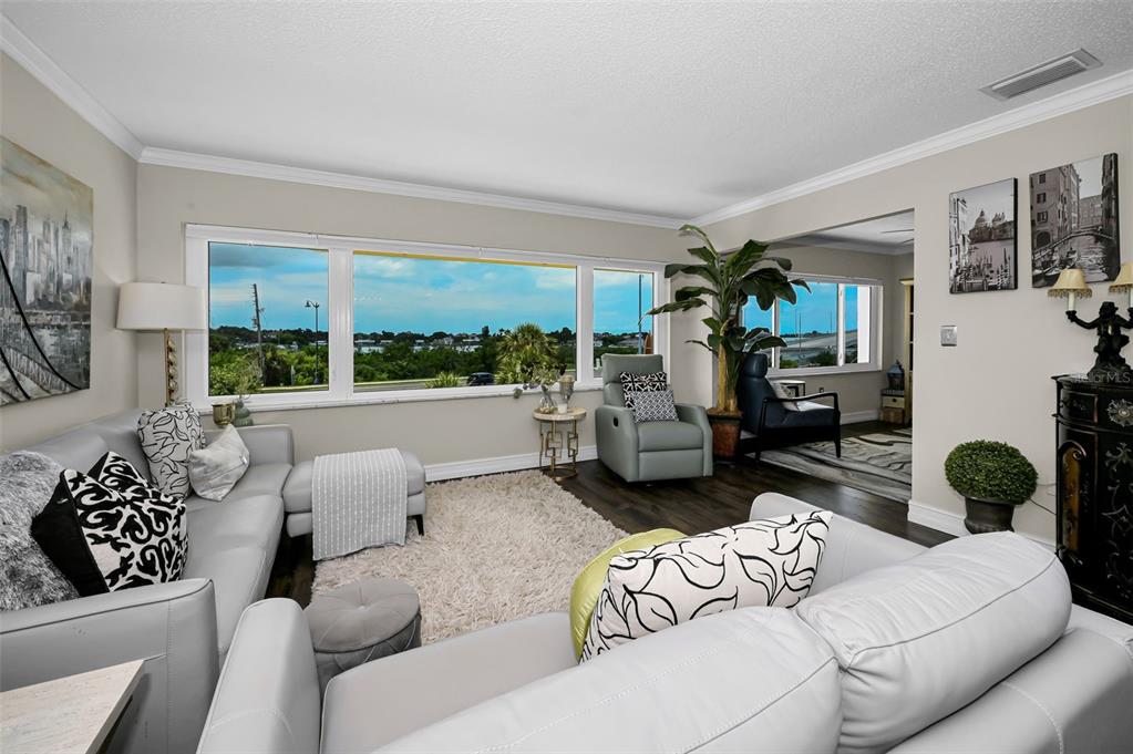 A living room features light gray sofas, a white shag rug, and large windows with views — 100 BLUFF VIEW DRIVE UNIT 211C, BELLEAIR BLUFFS, FL