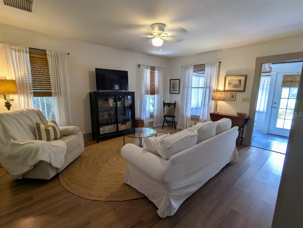A living room features a white sofa, an armchair, a television, and hardwood flooring — 7427 CHAPEL AVENUE, NEW PORT RICHEY, FL