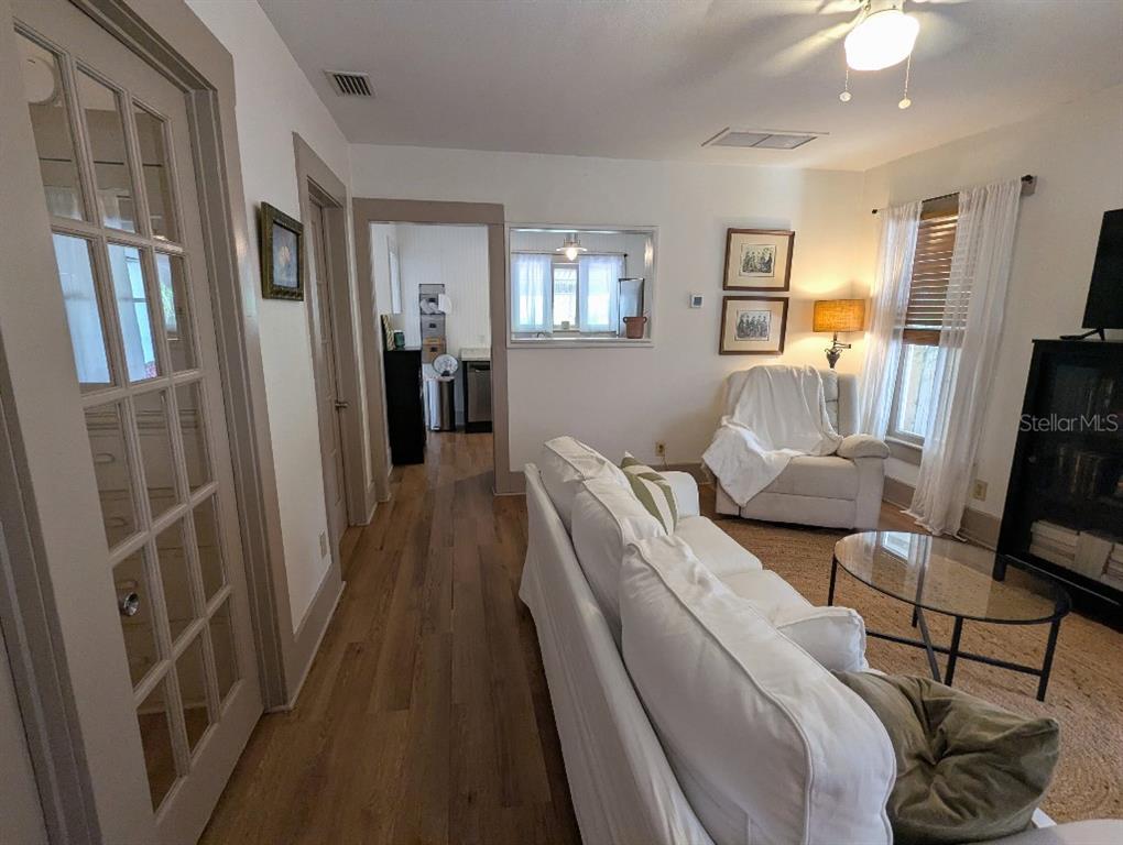 A living room features white furniture, hardwood floors, and a doorway leading to a kitchen — 7427 CHAPEL AVENUE, NEW PORT RICHEY, FL