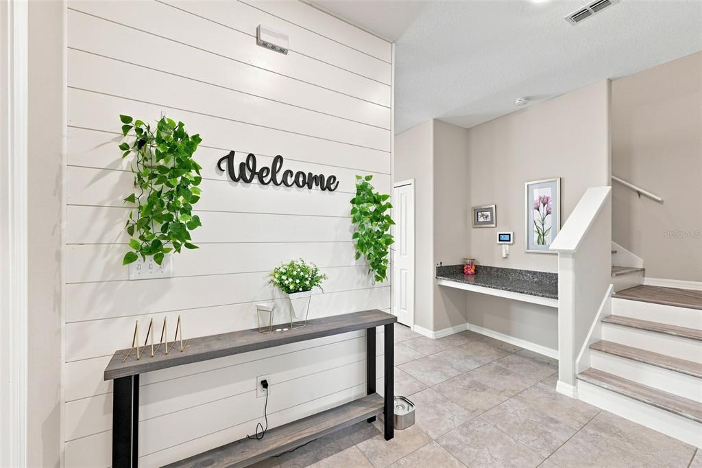 A foyer features a shiplap wall with a console table, hanging plants, and a staircase — 15548 FLORENCE HOLLOW PLACE, SUN CITY CENTER, FL