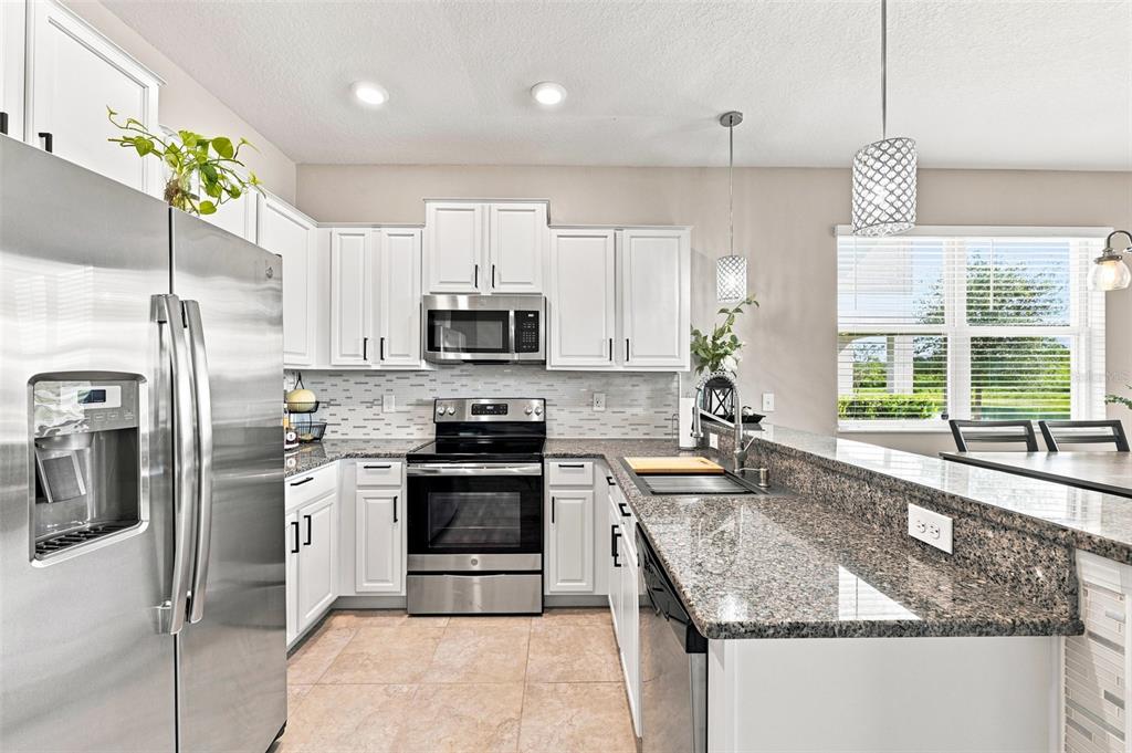A kitchen features white cabinets, granite countertops, stainless steel appliances, and tile flooring — 15548 FLORENCE HOLLOW PLACE, SUN CITY CENTER, FL