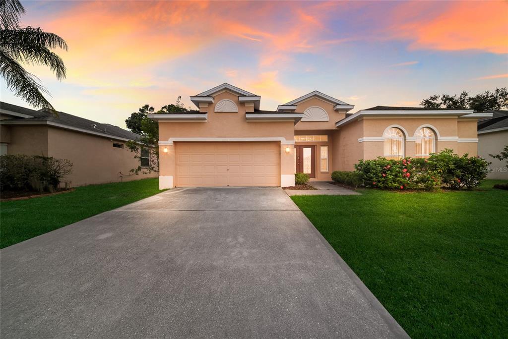 A single-story peach-colored house with a two-car garage and a concrete driveway at sunset — 230 41ST STREET NE, BRADENTON, FL