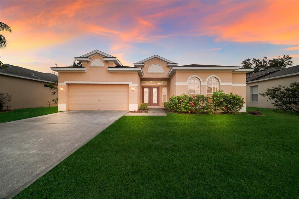 A single-story peach-colored house with a two-car garage and a front lawn at sunset — 230 41ST STREET NE, BRADENTON, FL
