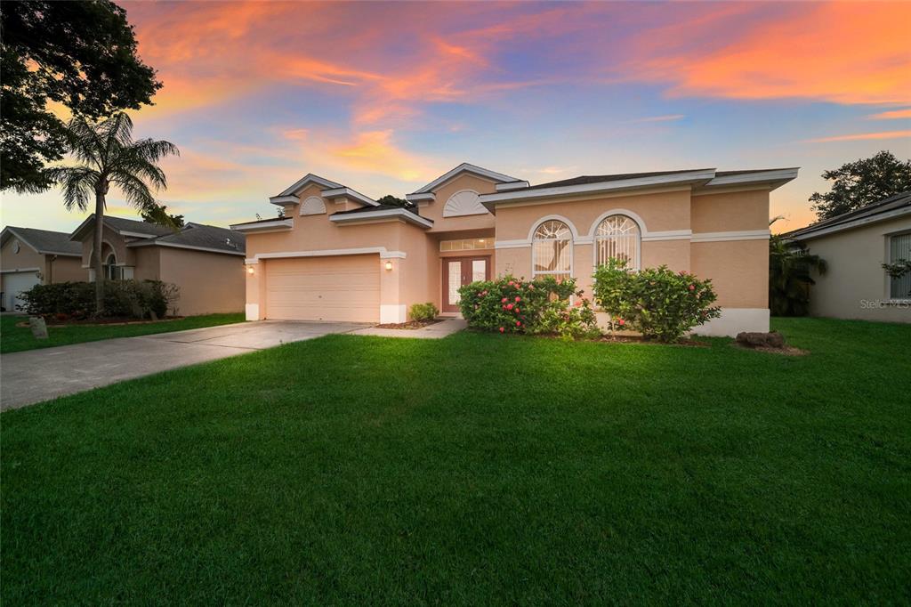 A single-story peach-colored house with a two-car garage and arched windows under a sunset sky — 230 41ST STREET NE, BRADENTON, FL