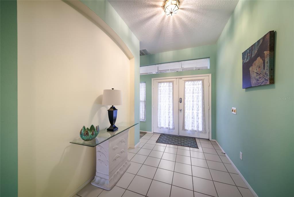 An entryway features a glass-topped console table, tile flooring, and double doors with white curtains — 230 41ST STREET NE, BRADENTON, FL
