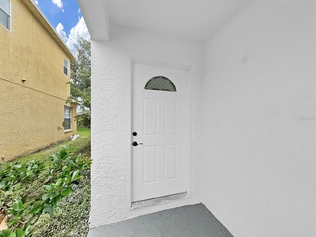 A white exterior door with a small arched window sits on a covered concrete porch — 1612 PROWMORE DR, BRANDON, FL