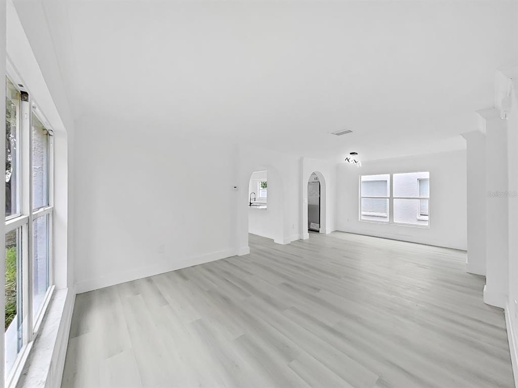 An empty living room features white walls, light wood-look flooring, and arched doorways — 1612 PROWMORE DR, BRANDON, FL