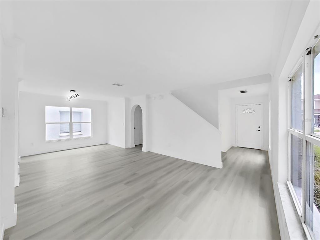 An empty living room features white walls, light wood-look flooring, and a white front door — 1612 PROWMORE DR, BRANDON, FL