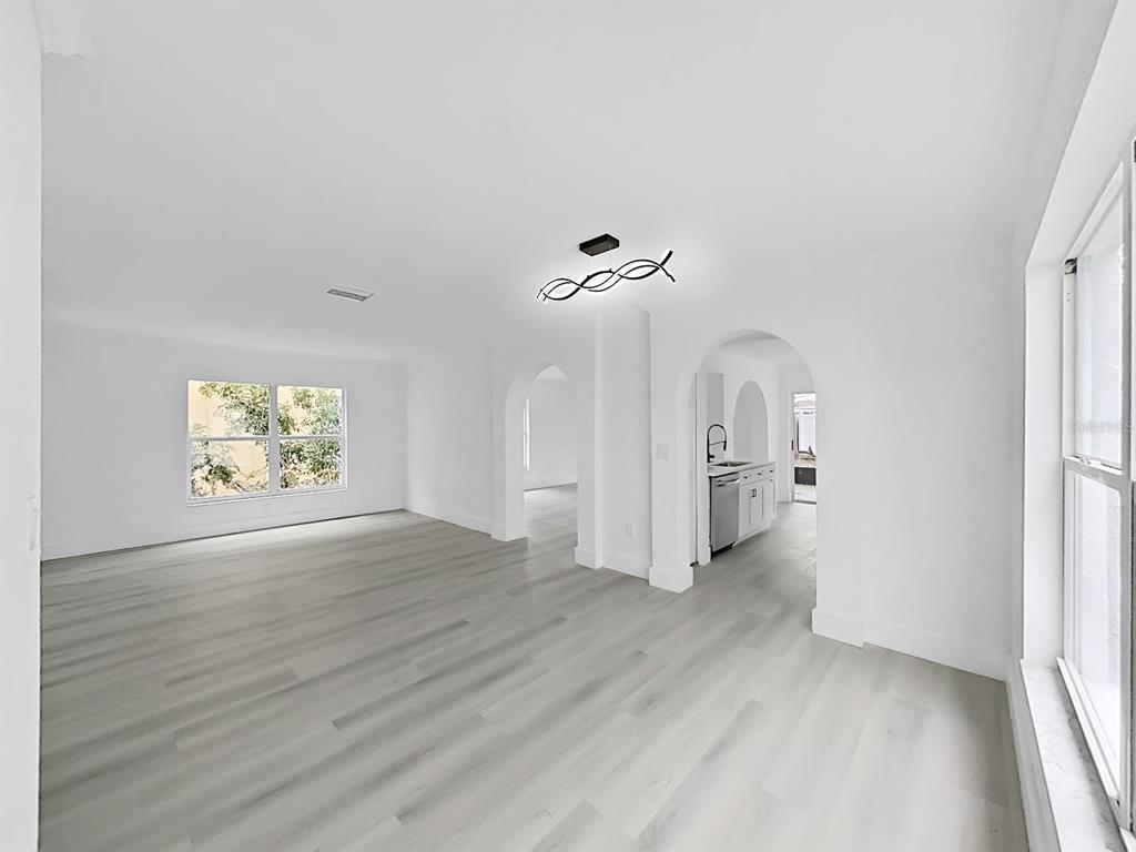 A bright, open-concept living area with light wood-look flooring and two arched doorways — 1612 PROWMORE DR, BRANDON, FL