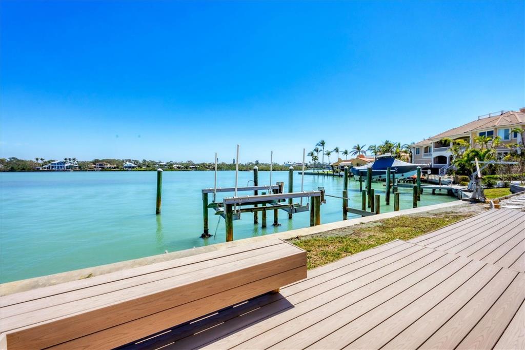 A wooden deck with a built-in bench overlooks a calm bay with boat docks — 919 KEY WAY, NOKOMIS, FL