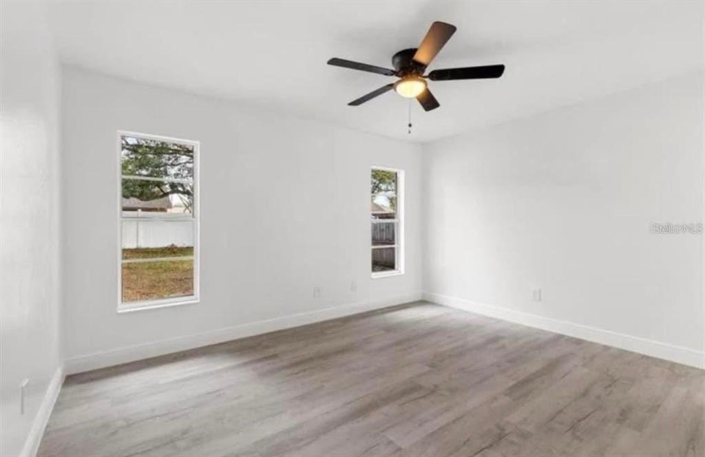 An empty bedroom with white walls, light wood-look flooring, two windows, and a ceiling fan — 14915 GENTILLY PLACE, TAMPA, FL