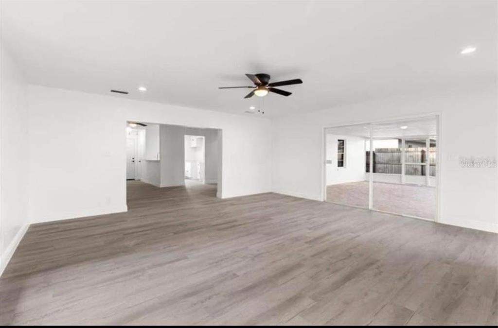 A spacious living room with light wood-look flooring, white walls, a ceiling fan, and sliding doors — 14915 GENTILLY PLACE, TAMPA, FL