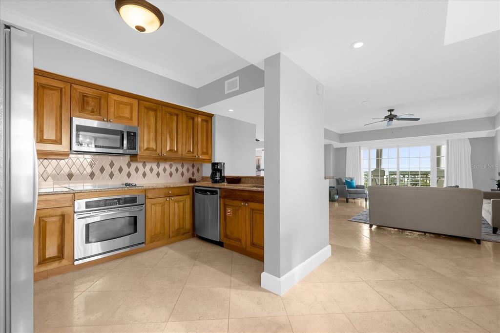 A kitchen with wood cabinets and stainless steel appliances opens into a bright living area — 7593 GATHERING DRIVE UNIT 608, REUNION, FL