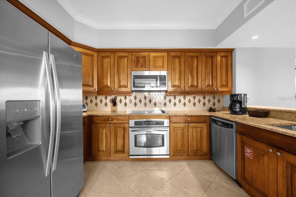 A kitchen features wood cabinets, stainless steel appliances, granite countertops, and a diamond-patterned tile backsplash — 7593 GATHERING DRIVE UNIT 608, REUNION, FL