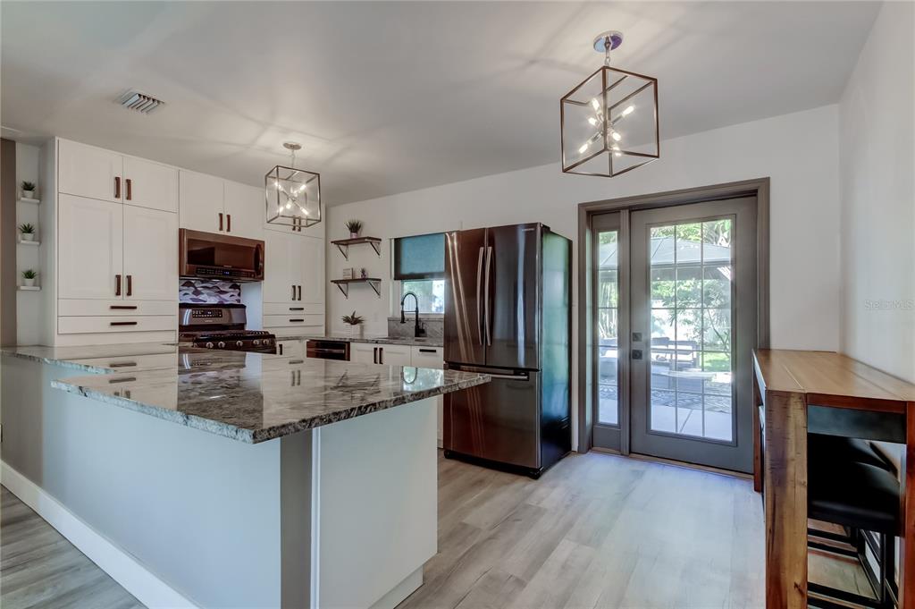 A modern kitchen features white cabinetry, granite countertops, stainless steel appliances, and a glass-paned door — 375 10TH AVENUE N, SAFETY HARBOR, FL