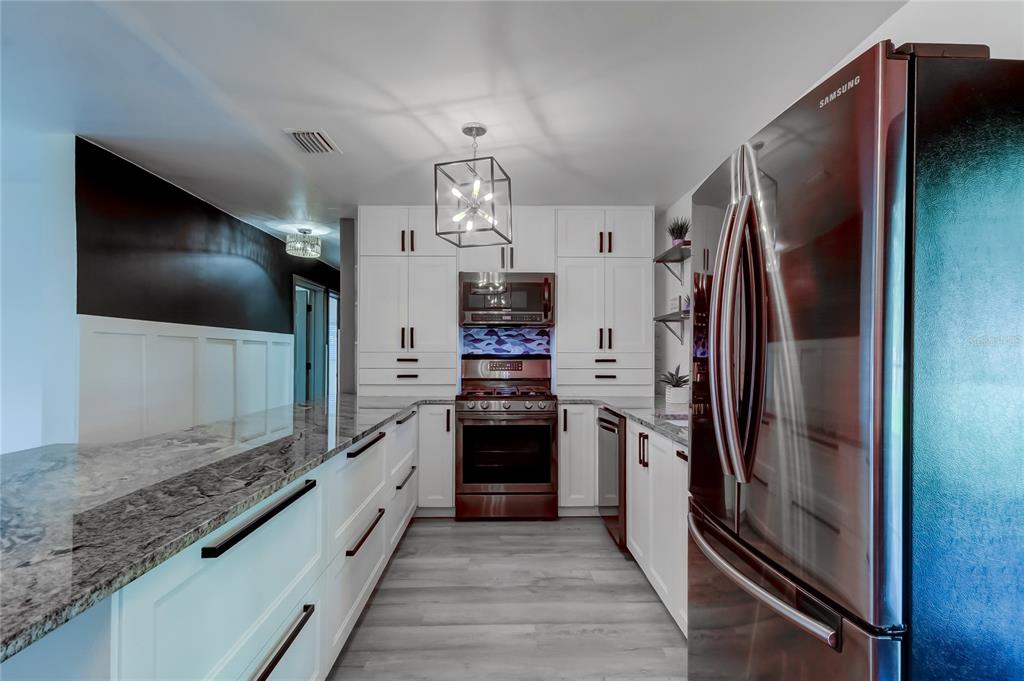 A kitchen features white cabinetry, dark granite countertops, stainless steel appliances, and light wood flooring — 375 10TH AVENUE N, SAFETY HARBOR, FL