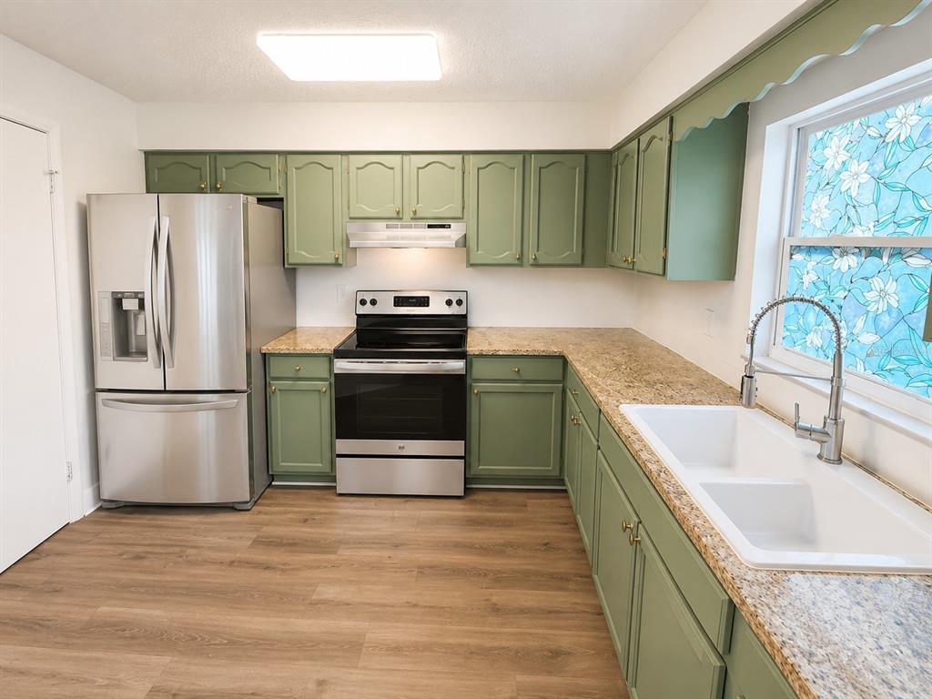 A kitchen with sage green cabinets, granite countertops, stainless steel appliances, and wood-look flooring — 7313 THOMAS JEFFERSON CIRCLE E, BARTOW, FL