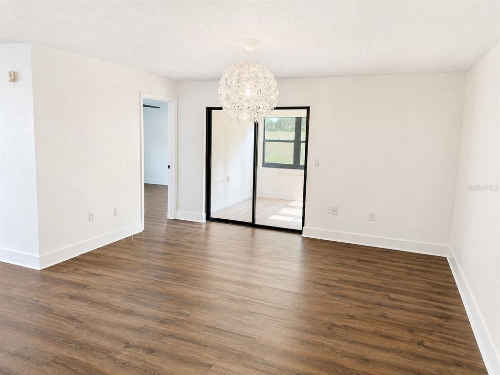 An empty room with wood-look flooring, white walls, a modern pendant light, and sliding glass doors — 7313 THOMAS JEFFERSON CIRCLE E, BARTOW, FL