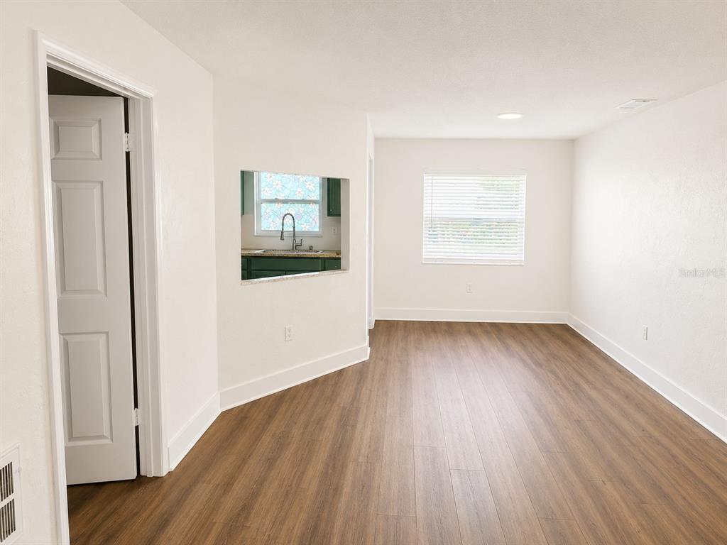 An empty room with wood-look flooring, white walls, and a pass-through window to the kitchen — 7313 THOMAS JEFFERSON CIRCLE E, BARTOW, FL