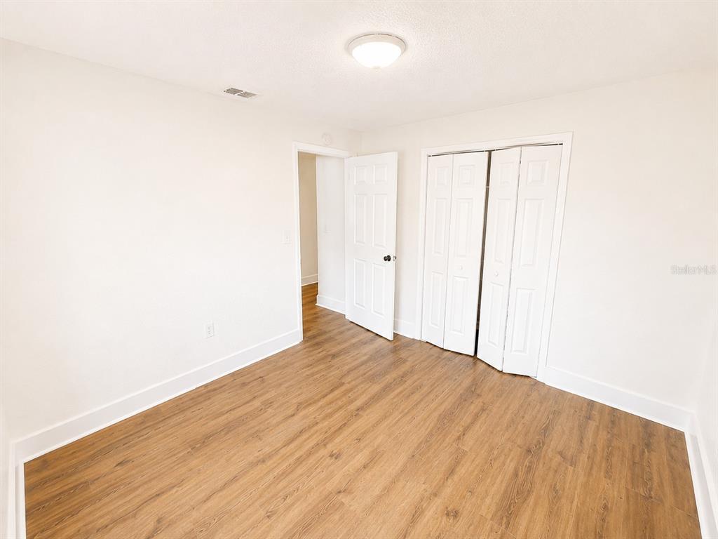 An empty bedroom features white walls, wood-look flooring, a closet with bifold doors, and a doorway — 7313 THOMAS JEFFERSON CIRCLE E, BARTOW, FL