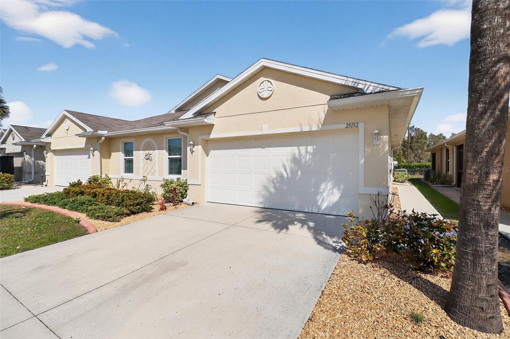 A beige single-story house features a two-car garage, a concrete driveway, and landscaped front beds — 25152 E LENOX CIRCLE, PUNTA GORDA, FL