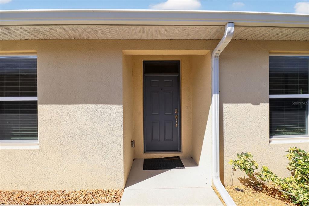 A front entryway features a dark gray door, a transom window, and a concrete porch — 25152 E LENOX CIRCLE, PUNTA GORDA, FL