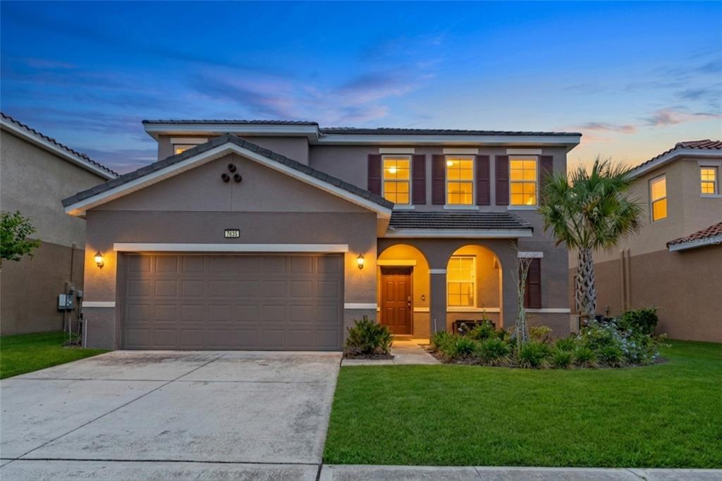 A two-story suburban house with a two-car garage, arched entryway, and a manicured front lawn — 7635 OAKMOSS LOOP, DAVENPORT, FL