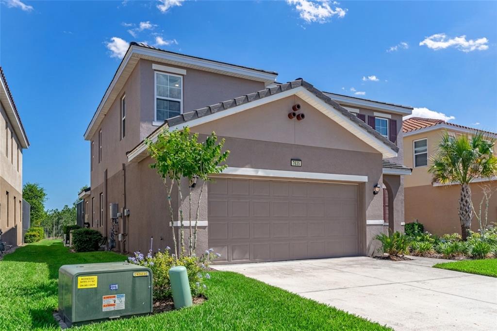 A two-story suburban house with a tan stucco exterior and a two-car garage — 7635 OAKMOSS LOOP, DAVENPORT, FL