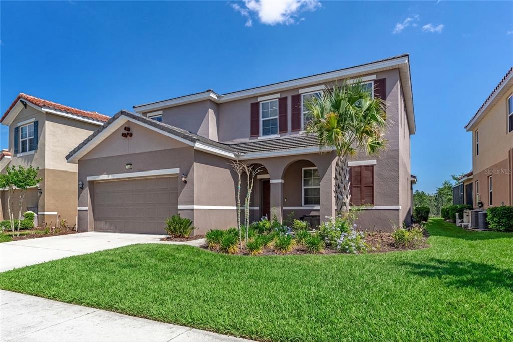 A two-story suburban house with a tan stucco exterior, a two-car garage, and a palm tree — 7635 OAKMOSS LOOP, DAVENPORT, FL