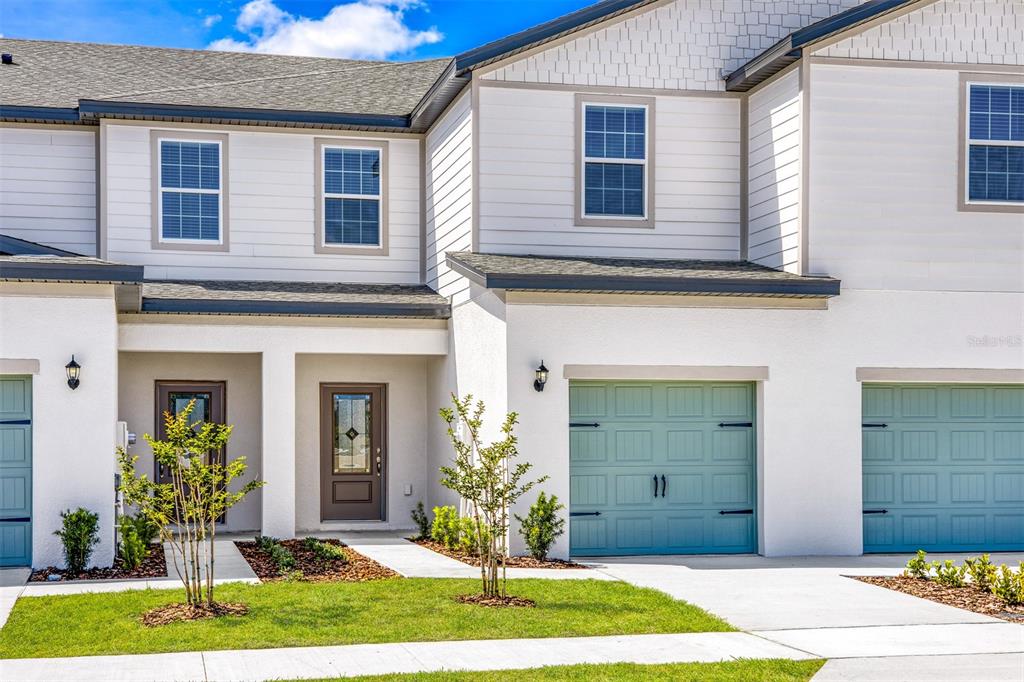 The exterior of a two-story townhouse features white siding, a brown front door, and blue garage doors — 709 POPPY LANE, DUNDEE, FL
