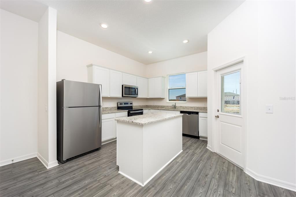 A kitchen with white cabinets, granite countertops, stainless steel appliances, and a center island — 709 POPPY LANE, DUNDEE, FL