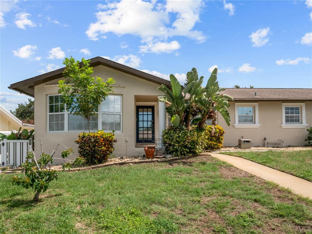A single-story house with a tan stucco exterior, a dark front door, and landscaping — 14331 APACHE AVENUE, LARGO, FL