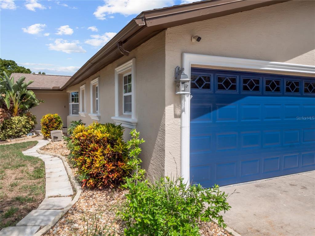 A side view of a house exterior featuring a blue garage door and landscaping — 14331 APACHE AVENUE, LARGO, FL
