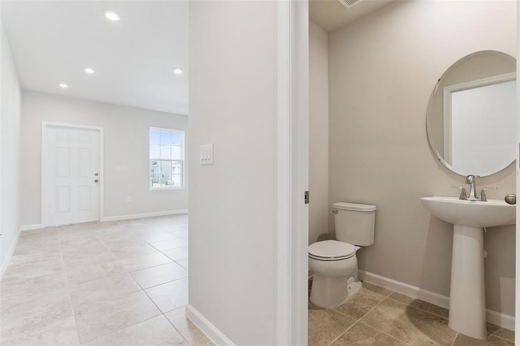 A view from a tiled room into a small bathroom with a pedestal sink and toilet — 1206 PORT BLUE WAY, LADY LAKE, FL