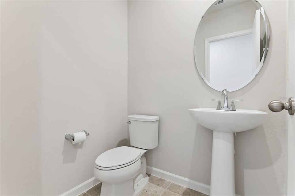 A small powder room features a pedestal sink, a round mirror, and a white toilet — 1206 PORT BLUE WAY, LADY LAKE, FL