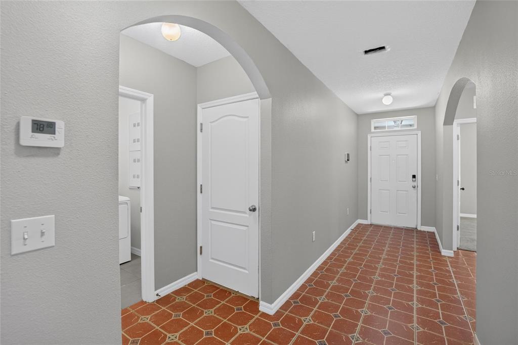 An entryway features terracotta-style tile flooring, gray walls, an arched doorway, and a white front door — 16441 TREASURE POINT DRIVE, WIMAUMA, FL