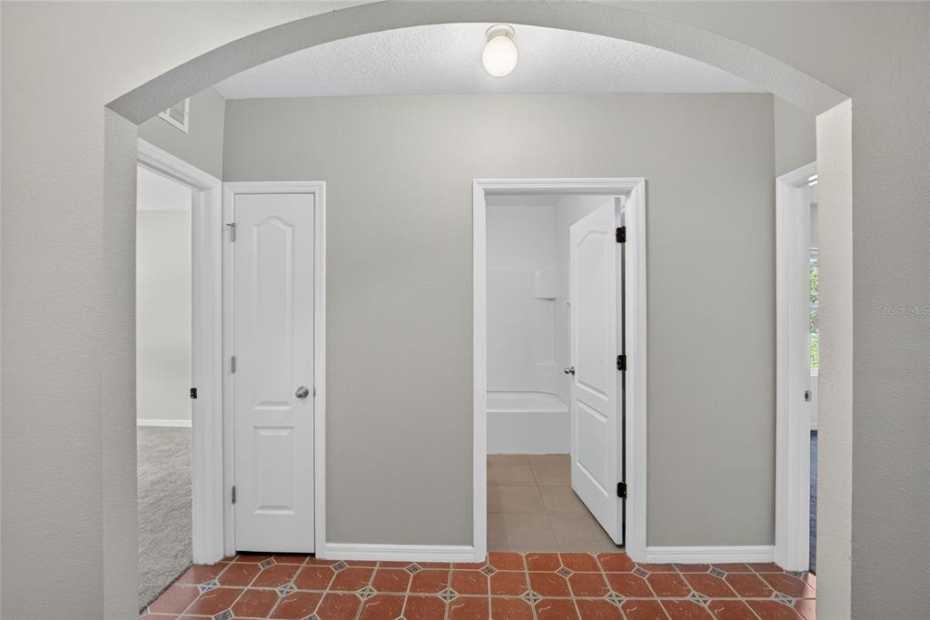 A hallway with terracotta tile flooring, gray walls, and three white interior doors — 16441 TREASURE POINT DRIVE, WIMAUMA, FL